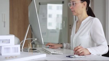 Profesyonel kadın, ofis çalışma alanındaki masasında teknoloji ve fiziksel modeller kullanarak mimari tasarımlar yaratmaya odaklandı. İş ve mimari kavramı