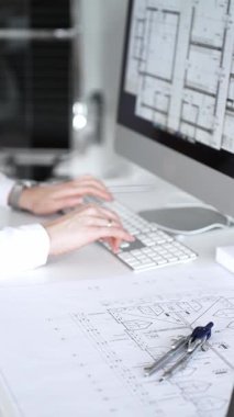 Bir bina projesi planlayan mimar veya mühendis, bir masaüstü bilgisayarındaki planları ve teknik çizimleri gözden geçiriyor. İş ve mimari kavramı
