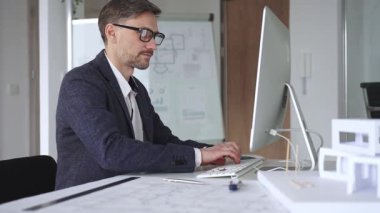 Erkek mimar, mimari bir stüdyoda yeni yapılar ve modeller tasarlayarak bilgisayar ekranına ve planlara derinden odaklanmıştır. İş ve mimari kavramı