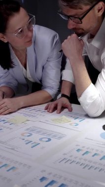 İş adamları masadaki mali belgeleri ve veri tablolarını inceliyor, çizelgeleri ve grafikleri analiz ediyor ve bir akşam ofis toplantısında kurumsal stratejiyi tartışıyorlar.