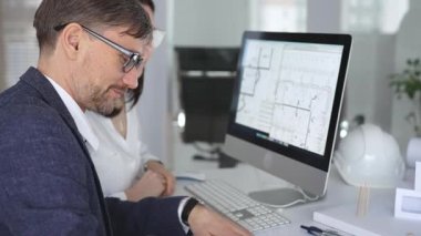 Mimarlar ve mühendisler birlikte çalışarak modern bir masaüstü bilgisayar ekranının planlarını tartışıyorlar. Takım çalışması ve tasarım süreci gösteriliyor. İş ve mimari kavramı