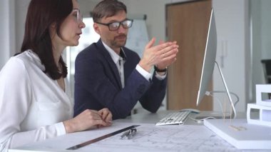 Mimarlar, modern ofis ortamında tasarım ayrıntıları ve inşaat planlarını tartışan planlar ve ölçekli bir model üzerinde işbirliği yapıyorlar. İş ve mimari kavramı