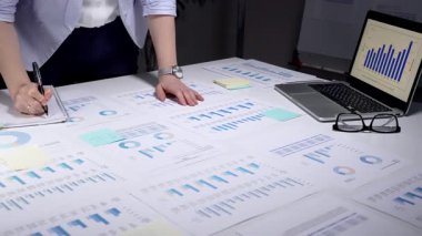 İş kadını kurumsal mali verileri analiz ediyor, istatistik ve pazar eğilimlerini yönetiyor, belgeleri inceliyor, yatırım stratejisi planlıyor, ofiste yıllık bir rapor üzerinde çalışıyor