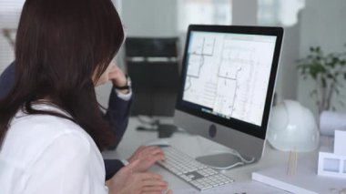 Yeni bir inşaat projesi üzerinde çalışan tasarım uzmanları, bir masaüstü bilgisayarında plan ve mimari çizimleri inceliyorlar. İş ve mimari kavramı