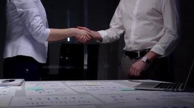 İş ortakları mali raporlar, çizelgeler, dizüstü bilgisayarlar ve not defterleriyle dolu bir masanın üzerinde el sıkışırken, işbirliği, güven ve büyümeyi sembolize eden bir anlaşma imzalandı.