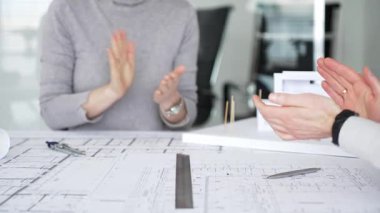 Ofis toplantılarında, bir grup iş adamı, masanın üzerindeki mimari planlar ve modellerle çevrili başarı ve başarıları alkışlıyor ve seviniyor.
