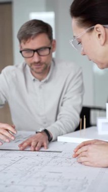 Mimari planlar ve inşaat planları üzerinde işbirliği yapan mimarlar, mühendislik projesinin detaylarını tartışan, bir ofiste tasarım araçları ve dijital tablet kullanan mimarlar