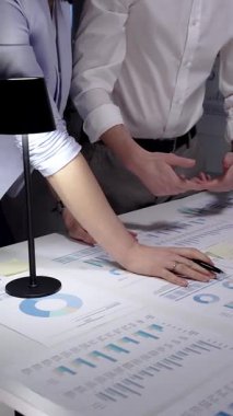 İş adamları masadaki mali belgeleri ve veri tablolarını inceliyor, çizelgeleri ve grafikleri analiz ediyor ve bir akşam ofis toplantısında kurumsal stratejiyi tartışıyorlar.