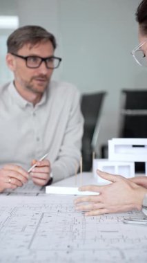 Mimari planlar ve inşaat planları üzerinde işbirliği yapan mimarlar, mühendislik projesinin detaylarını tartışan, bir ofiste tasarım araçları ve dijital tablet kullanan mimarlar