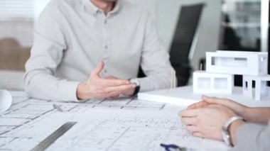 Mimarlar planları ve mimari modelleri inceliyor, profesyonel bir ofis toplantısında tasarım ve şehir planlamasını tartışıyor, gelecekteki inşaat projeleri üzerinde işbirliği yapıyor, kapatıyorlar.