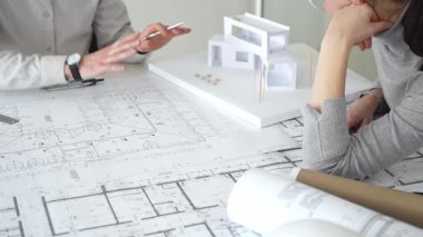 İki mimar yeni bir bina tasarımında işbirliği yapıyor ayrıntılı planları gözden geçiriyorlar ve pusula ile beyaz bir mimari modelin yanındaki planları titizlikle ölçüyorlar.