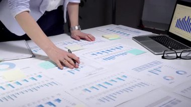 İş kadını kurumsal mali verileri analiz ediyor, istatistik ve pazar eğilimlerini yönetiyor, belgeleri inceliyor, yatırım stratejisi planlıyor, ofiste yıllık bir rapor üzerinde çalışıyor