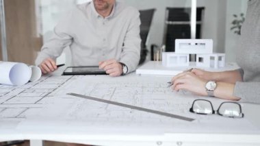 Mimari planlar ve inşaat planları üzerinde işbirliği yapan mimarlar, mühendislik projesinin detaylarını tartışan, bir ofiste tasarım araçları ve dijital tablet kullanan mimarlar