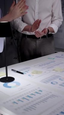 Karanlık bir ofiste el çırpan iş adamları, veri tabloları, finansal grafikler ve çalışan dizüstü bilgisayarlarla çevrili bir gece geç saatlerde yapılan toplantıda elde edilen başarıları kabul ediyorlar.