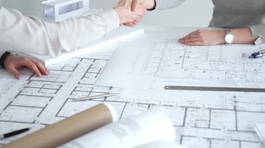 Bir ortaklık kuran iş adamları, mimari planları ve bina modelini el sıkışarak, başarılı bir anlaşmayı ve inşaat endüstrisindeki işbirliğini sembolize ederek,