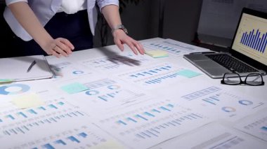 İş kadını kurumsal mali verileri analiz ediyor, istatistik ve pazar eğilimlerini yönetiyor, belgeleri inceliyor, yatırım stratejisi planlıyor, ofiste yıllık bir rapor üzerinde çalışıyor