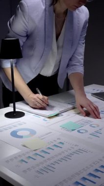 Finansal verileri yöneten iş kadını, gece geç saatlerde raporları analiz eden, laptopta fazla mesai yapan, karanlık bir ofiste masa başında duran, stratejik planlamalara konsantre olan..