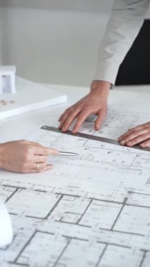 Mimarlar yeni bina tasarımını tartışıyor, ayrıntılı planların üzerinde bir pusula tutuyor, modern bir ofis düzeninde ev mimarisi modeliyle proje geliştirmede işbirliği yapıyor,