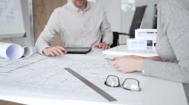 Mimari planlar ve inşaat planları üzerinde işbirliği yapan mimarlar, mühendislik projesinin detaylarını tartışan, bir ofiste tasarım araçları ve dijital tablet kullanan mimarlar
