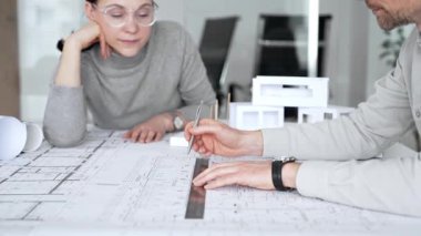 Mimarlar inşaat planlarını ve 3D yapı modelini gözden geçiriyorlar, profesyonel ofis ortamında yeni bir mimari proje üzerinde çalışırken ayrıntılı bir tasarım tartışmasına girişiyorlar.