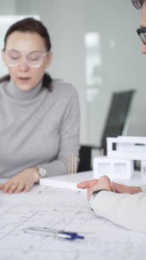 Planlar üzerinde işbirliği yapan mimarlar, kadın bir meslektaşın gözlemlediği gibi planları ölçmek için pusula kullanan bir erkek tasarımcı, proje detayları ve mimari tasarımı tartışan,