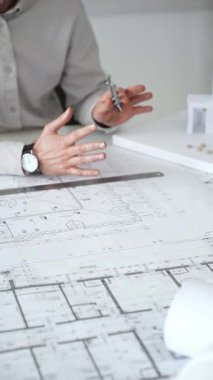 Mimarlar detaylı planlar ve beyaz bir masanın üzerinde bir ölçek modeli etrafında toplanarak, modern bir konut projesinde işbirliği yaparken planları analiz ediyor, araçlar ve belgeler çiziyor ve kapatıyorlar.