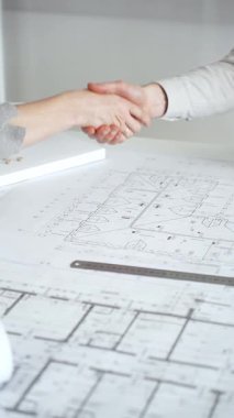 Bir ortaklık kuran iş adamları, mimari planları ve bina modelini el sıkışarak, başarılı bir anlaşmayı ve inşaat endüstrisindeki işbirliğini sembolize ederek,