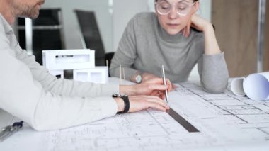 Mimarlar inşaat planlarını ve 3D yapı modelini gözden geçiriyorlar, profesyonel ofis ortamında yeni bir mimari proje üzerinde çalışırken ayrıntılı bir tasarım tartışmasına girişiyorlar.