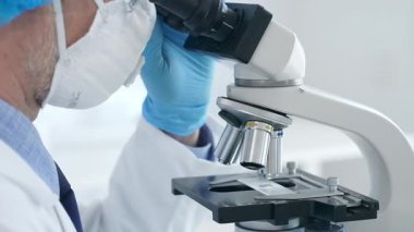 Laboratuvarda mikroskop ayarlayan mavi eldivenli erkek bilim adamlarına yakın çekim, bilimsel araştırma ve analiz yapıyorlar. Tıp ve bilim konsepti.