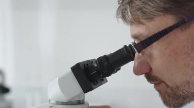 Bir erkek bilim adamının mikroskopla bakıp laboratuvar ortamında araştırma ve analiz yapması bilimsel araştırma ve keşifler sergilemesi. Tıp ve bilim konsepti.