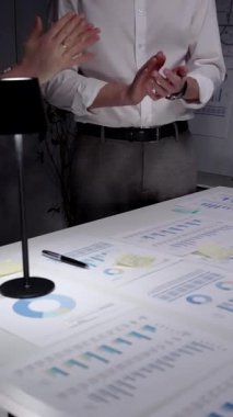 Karanlık bir ofiste el çırpan iş adamları, veri tabloları, finansal grafikler ve çalışan dizüstü bilgisayarlarla çevrili bir gece geç saatlerde yapılan toplantıda elde edilen başarıları kabul ediyorlar.