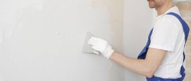 Profesyonel inşaat işçisi mavi tulum ve beyaz eldiven giyerek bir daireye beyaz bir duvar örüyor.