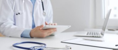 Mavi steteskopun kapatılması, dijital tablet reçetesini inceleyen ve çağdaş tıbbi ortamda dijital sağlık hizmeti akışını temsil eden kadın doktorun yanındaki masada yatıyor. İlaç..