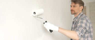 Kareli gömlek giyen profesyonel bir ressam, apartman duvarına boya rulosu ile beyaz boya sürüyor. Geniş kapsamlı ev yenileme çalışmaları sırasında iç mekanı sürekli darbelerle değiştiriyor..