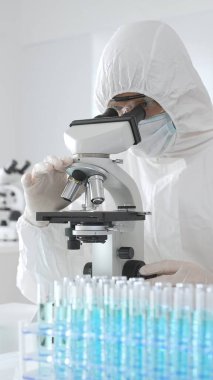 Koruyucu ekipman alanında çalışan bir tıp virologu laboratuvar ortamında araştırma yaparken mikroskop altında virüs örneklerini inceliyor..