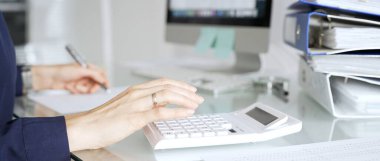 Modern bir ofis masasında beyaz hesap makinesiyle rakamları hesaplayan bir kadın. Şirket finans, vergi ve muhasebe işlerini yönetiyor. İş dünyasında denetim ve vergi teması