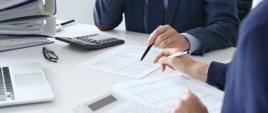 Erkek muhasebeci finansal belgeleri analiz ediyor, ortak çalışma alanındaki rakamları hesaplıyor ve onları çevreleyen dizüstü bilgisayar ve ofis malzemeleriyle birlikte. Denetim ve vergi kavramı.