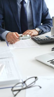 Erkek mali analistler, işyerindeki kurumsal verileri incelerken büyüteç ve hesap makinesi kullanarak belgeleri inceliyorlar. Denetim ve vergi kavramı.