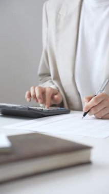 Yıllık vergisini hesaplayan profesyonel muhasebeci, mali belgeleri gözden geçiren, iş yerindeki bütçe detaylarını hesap makinesi ve evrak işleriyle takip eden. Ticarette denetim ve vergiler