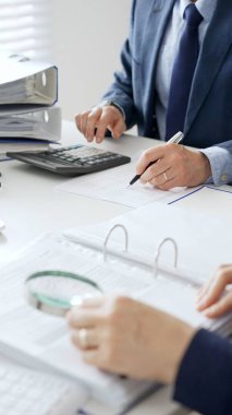 Ekonomik belgeleri analiz eden, hesap makineleri ve dizüstü bilgisayarlar kullanan iş adamları modern ofiste proje üzerinde birlikte çalışıyorlar. Denetim ve vergi kavramı.