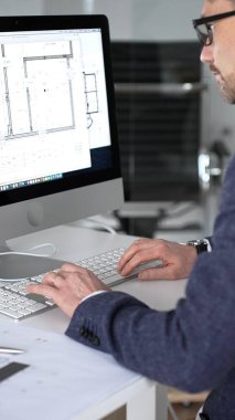 Modern ofiste klavyede yazan profesyonel mimar, planlar, ölçek modelleri ve tasarım araçları ile çevrili, planlama projesi. İş ve mimari kavramı