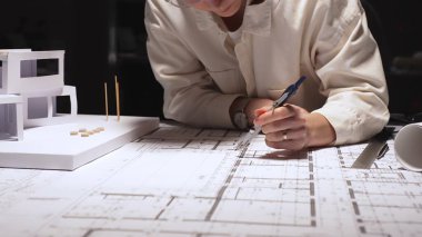 Profesyonel mimar, masa üzerinde pusula ve ölçekli ayrıntılı planlar hazırlıyor, modern ev inşaatını hassasiyetle ve yaratıcılıkla planlarken konut modelini gözden geçiriyor.