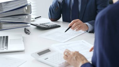 Erkek muhasebeci finansal belgeleri analiz ediyor, ortak çalışma alanındaki rakamları hesaplıyor ve onları çevreleyen dizüstü bilgisayar ve ofis malzemeleriyle birlikte. Denetim ve vergi kavramı.