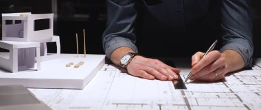 Experienced architect at desk combining traditional drafting tools and laptop to study detailed blueprints, focusing on precision and planning for residential and commercial projects