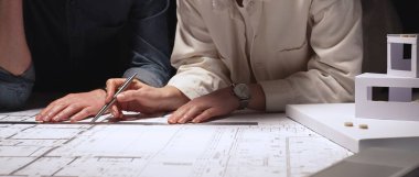 Mimarlık uzmanları teknik planları analiz ediyor ve yeni bir şehir gelişimi tasarlamak için taslak araçları kullanıyorlar. Yakınlardaki ölçekli bir modelle inşaat planlama ve mühendislik tasarımına odaklanıyor.