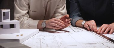 Mimarlık uzmanları teknik planları analiz ediyor ve yeni bir şehir gelişimi tasarlamak için taslak araçları kullanıyorlar. Yakınlardaki ölçekli bir modelle inşaat planlama ve mühendislik tasarımına odaklanıyor.