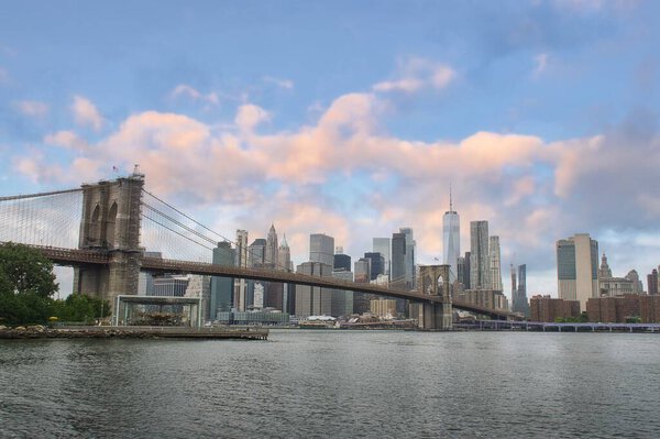 Stunning view of Manhattan skyline and Brooklyn bridge with sunset clouds in New York City, USA