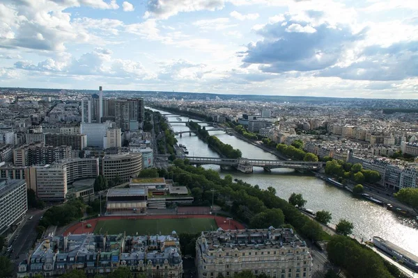 A panoramic aerial view of Paris skyline including river Seine lined with boats, a golden doom of Palace of invalides and other historical monuments, parks and gardens