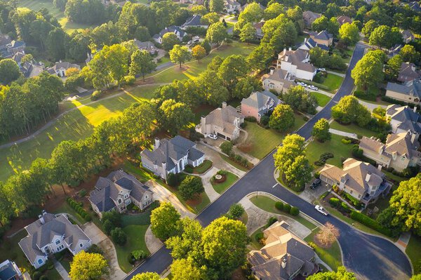 Aerial view of beautiful houses, roofs and lush green landscaped yards in an upscale subdivision in suburbs of USA shot during Golden hour during early spring.