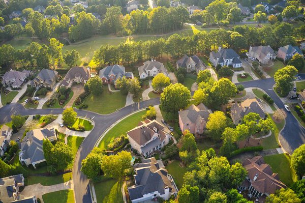 Aerial view of beautiful houses, roofs and lush green landscaped yards in an upscale subdivision in suburbs of USA shot during Golden hour during early spring.